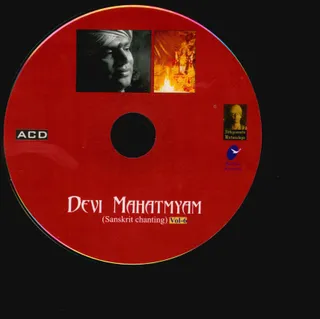 Red CD disc labelled 'Devi Mahatmyam (Sanskrit chanting) Vol-6' with a black-and-white portrait of a man in a light turban at upper left and a small colour photo of a deity murti with a fire pit and oil lamps at upper centre. A small gold-toned 'a person Kirtanalaya' badge and a blue bird logo sit at the right edge. The disc is a graphic product image, with no physical people present.