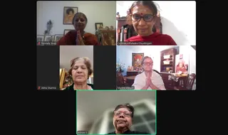 A video-call grid of five women participating remotely, each in a separate tile labelled with a name. Top left, Nirmala Sivaji wears a red top and presses her palms together in anjali beside framed pictures. Top right, Ca Shakunthaladevi Dayalingam wears red and has a bindi and tilak, with a red-cushioned wooden chair behind her. Middle left, Abha Sharma sits with eyes closed and hands out of view in a green top beside a shelf with small figurines. Middle right, Martha Watson wears white and presses her palms together in anjali in a room with a framed deity picture, a wooden cabinet and a seated saffron-robed figure on a throne-like seat. Bottom centre, Indrani S wears a black top with a red bindi and smiles with hands held in front. Tile names are printed on the screen.