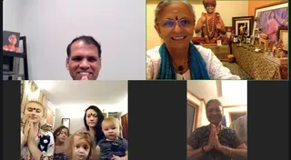 A four-panel video call collage of a virtual KAILASA OHIO, USA yoga and Nithya Puja session. Top left, a smiling man in a grey-walled room with a framed portrait on a shelf. Top right, a smiling woman with grey hair, a tilak and blue glasses wears a white top, a teal shawl and beaded malas, sitting before a home altar with a framed image of a saffron-robed, rudraksha-garlanded figure, a deity picture and oil lamps. Bottom left, a group of women and children stand in a living room, one young woman with a bindi holding her palms together in anjali. Bottom right, an older woman in a patterned dark top smiles with palms joined in namaste. The panels show a devotional online gathering; no physical persons count beyond those visible.