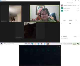A screenshot of a Zoom meeting with three video tiles and a participants panel listing three participants. The top-right tile shows a smiling woman with a red bindi and headphones in front of a framed picture of a deity, with a small image visible beside her. The top-left tile shows a woman with dark hair looking upward in a bright room, and the lower tile shows a woman with dark hair in a dim room. The Windows taskbar at the bottom shows a 5:28 AM clock dated 2/6/2021, and a dark overlay panel sits below the meeting window.