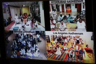 A screen showing a four-panel video link of live satsang sessions, each panel labelled with a location. Top left, labelled Guadeloupe-Rameshwaram, shows several people in white and orange clothes seated on a mat in a room with a curtain. Top right, labelled HYDERABAD AADHEENAM and Nithyananda-Nagaram-Hyderabad, shows people seated on mats, including a man in a white shirt and red shawl and a woman in white. Bottom left, labelled SAN JOSE AADHEENAM and San Jose-Madurai, shows a large group in white clothes seated in meditation posture on mats. Bottom right, labelled Los Angeles Aadheenam and LA-Arunachala, shows a group in white and red shawls seated on a striped rug, with a man in a dark shirt at the front right.