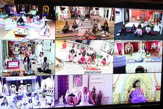 A nine-panel video-conference collage displayed on a screen, each panel showing a different centre where people sit in meditation or satsang. Panels are labelled with signs such as "SAN JOSE MADURAI", "OHIO PRAYAG", "NEW YORK VARANASI", "SINGAPURAM", "PHOENIX ANCHEEPURAM" and "VICTORIA AUSTRALIA". Participants wear white, pink and saffron clothing and sit on mats before decorated deity murti altars with garlands and drapes. Other panels show a seated man in a white tank top meditating before a small altar, and women in saris seated in rows.
