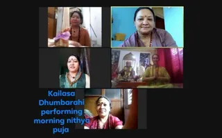 A video call screenshot in a five-panel grid of women participating in a remote online puja session. Top-left, a woman in an orange sari with rudraksha mala holds a tray with a pink flower. Top-right, a smiling woman in a lavender top and red-beaded mala. Middle-left, a woman in a green top with a red bindi and rudraksha necklace. Middle-right, a woman in a yellow sari with palms pressed in namaste beside a shrine with a deity murti and garlands. Bottom, a woman in a red blouse with a red bindi and mala sits in a doorway. Blue caption text reads Kailasa Dhumbarahi performing morning nithya puja.