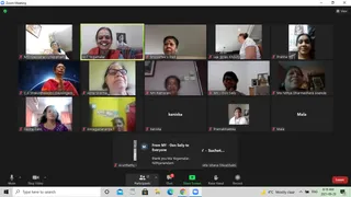 A Zoom video meeting screenshot showing a gallery grid of about seventeen participant tiles, mostly women in home settings. Tiles are labelled with names such as "A17 Yogamalar", "Lea Ikhlas Khoury", "Abha Sharma", "Slesha Dalvi", "kaniska", "Mala" and "Premabhaktika". One woman in a red shawl smiles in the top centre tile, another in the centre-left wears a red top and pressed hands, and a woman in a blue shirt gestures in the bottom left. Framed pictures and shelves appear behind several participants. The Zoom toolbar with Mute, Stop Video, Participants, Chat, Share Screen and Record is visible along the bottom, with a chat bubble reading "thank you Ma Yogamalar. Nithyanandam". The on-screen participants are not physically present in one room, so the scene has no physical people in a single location.